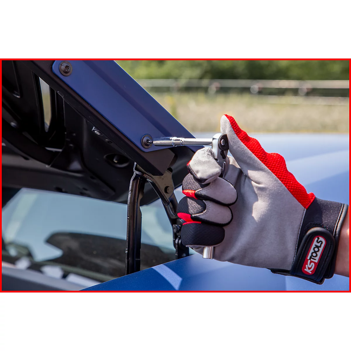 Hand in Arbeitshandschuh, der mit einem Werkzeug eine Schraube an einem blauen Karosserieteil festzieht.